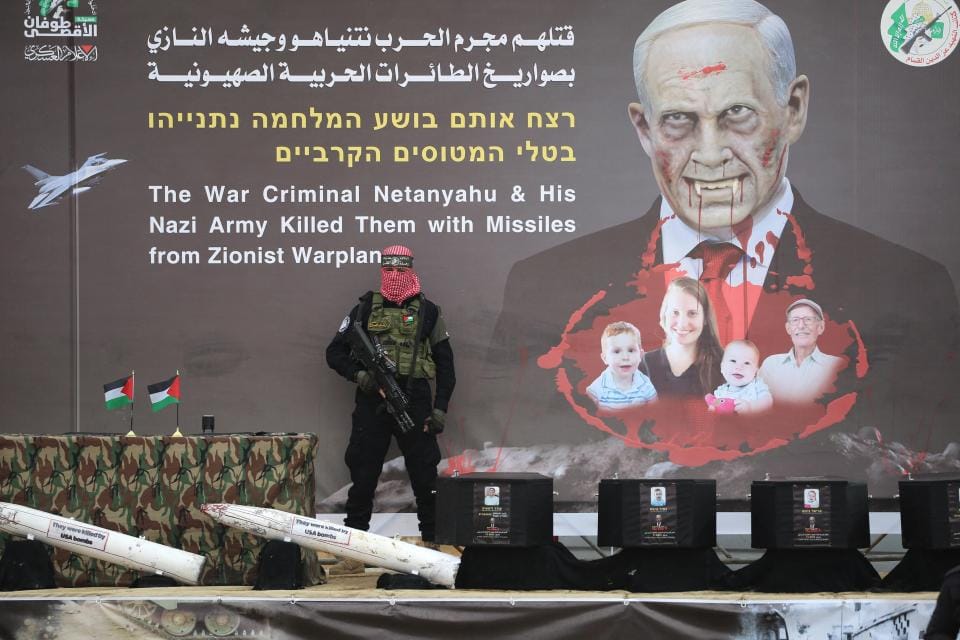 A Hamas fighter stands in front of a banner bearing an altered portrait of Israel's Prime Minister and the Bibas family, on stage ahead of the handing over the bodies of four Israeli hostages in Khan Yunis in the southern Gaza. Photo: AFP 